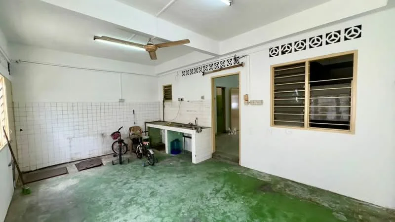 Room features: green concrete flooring, white painted walls, ceiling fan, window with metal grilles, sink with countertop, bicycle, small table, tiles on wall, door leading to another room.