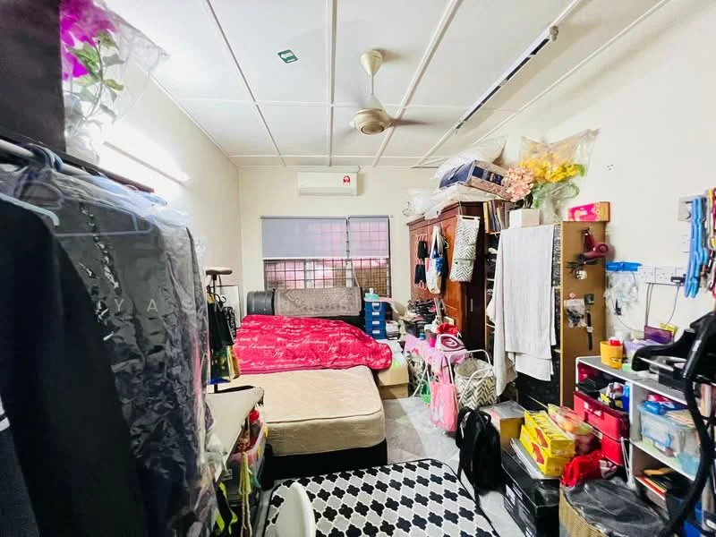 Bedroom features: queen-size bed with red bedding, single bed with beige bedding, wooden wardrobe, plastic storage boxes, ceiling fan, wall-mounted air conditioning unit, window with blinds, checkered area rug, clothes rack with hanging garments, shelves with various items, decorative flowers, wall-mounted mirror.