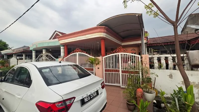 Exterior type: semi-detached house; features: white painted facade, red decorative accents, gated entrance with white metal gates, tiled porch area, manicured garden with potted plants, single-storey structure, car parked in driveway, overhanging roof, surrounded by residential buildings; style: traditional.