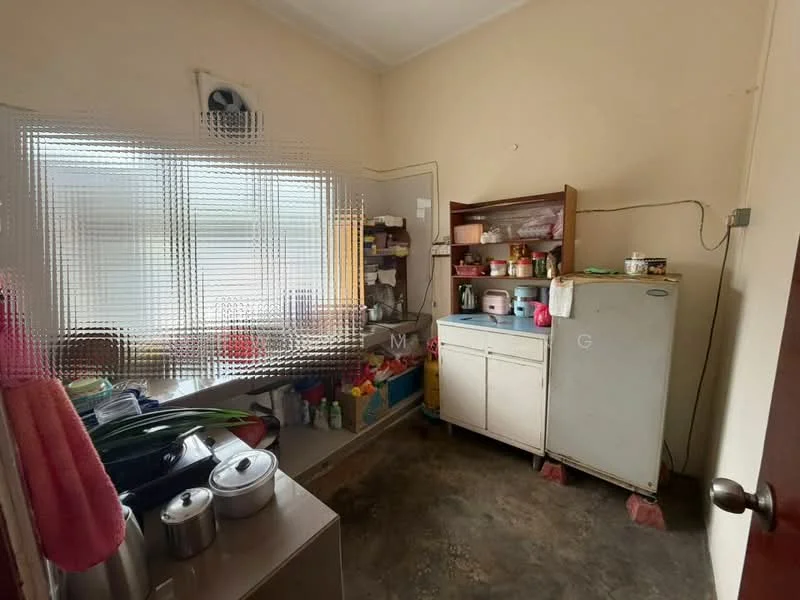 Kitchen features: white painted walls, concrete flooring, single-bowl stainless-steel sink, fridge, wooden shelving unit, various kitchen storage containers, window with sheer curtains, wall-mounted air conditioning unit.