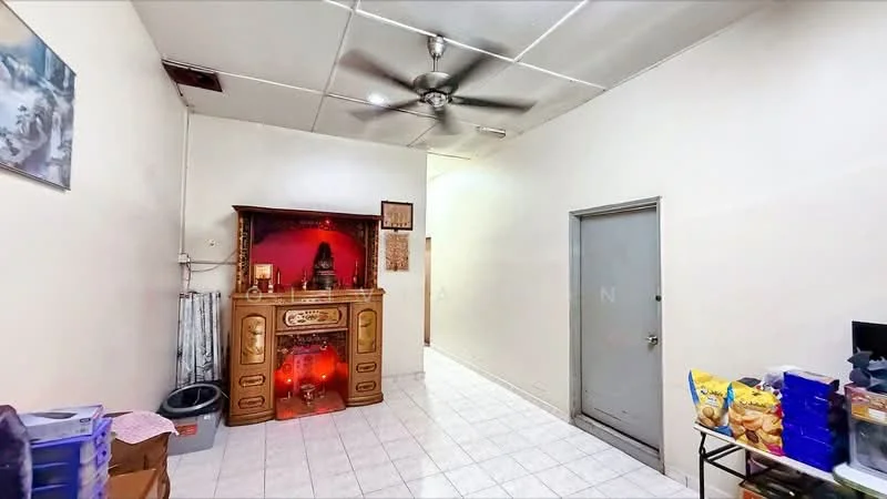 Room features: white painted walls, tile flooring, ceiling with fluorescent lights, 5-blade ceiling fan, wooden altar with decorative elements, doorway leading to another room, storage boxes, small table with snacks; style: minimalist.
