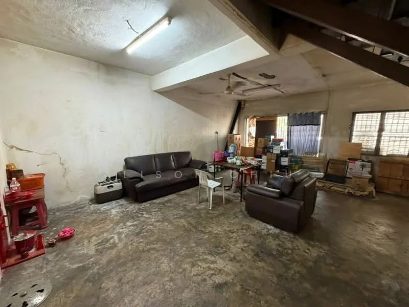 Living features: exposed concrete flooring, cream painted walls, ceiling fan, 2-seater leather sofa, 3-seater fabric sofa in dark brown, wooden storage cabinets, cardboard boxes, small white plastic chair, decorative items on table, window with black curtains.