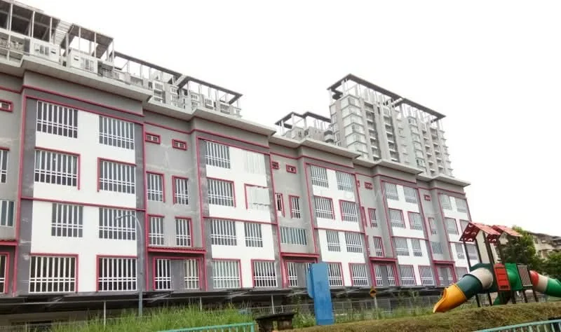 Exterior type: low-rise apartment block; features: grey painted facade, red accent trim, multiple floors, balconies on upper levels, large windows with vertical bars, playground equipment in foreground, manicured lawn, surrounding greenery; style: modern.