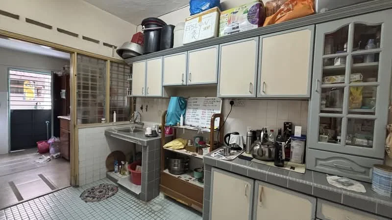 Kitchen features: light grey cabinetry with cream doors, stainless-steel sink, chrome faucet, tile backsplash, countertop with grey tiles, built-in shelves, open shelving with various containers, kitchen appliances including kettle and utensils, floor tiles in light blue, round area rug, window with sheer curtains; style: traditional. Room features: doorway leading to another room, visible floor tiles in light brown, open space with no defined features.