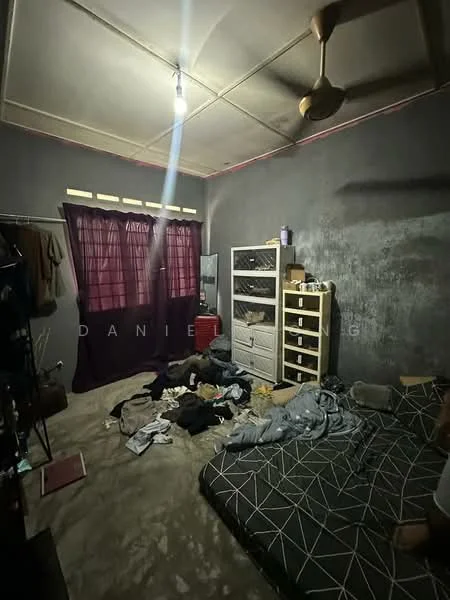 Bedroom features: grey painted walls, ceiling fan, single bed with patterned bedding, wooden wardrobe, plastic storage cabinet, curtains, carpeted flooring, clothes scattered on the floor.
