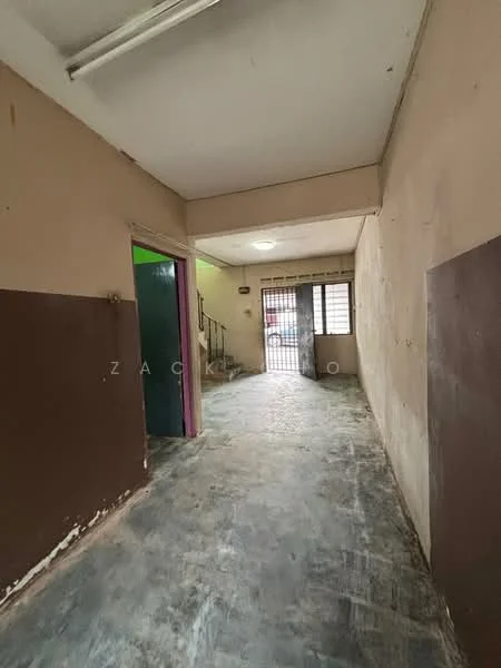 Room features: plain walls with brown and cream paint, concrete flooring, ceiling lights, doorway leading to another room, window with metal grille, staircase visible in the background; style: minimalist.