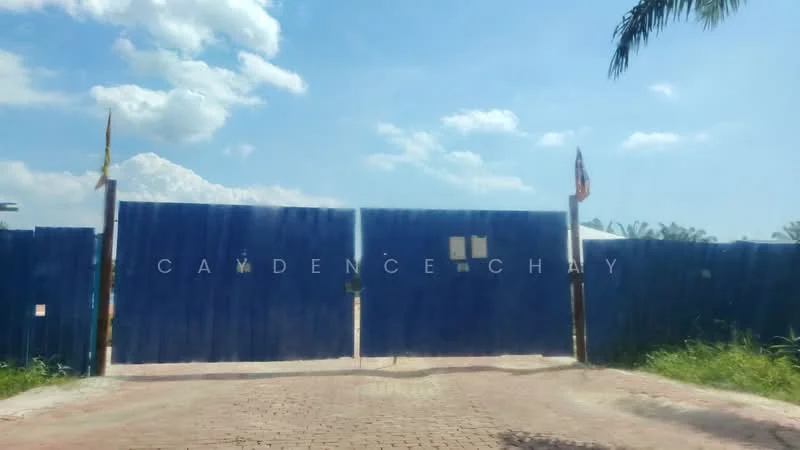 Exterior type: main entrance gate; features: blue painted gate, brick-paved driveway, surrounded by greenery, flagpole with flags, clear blue sky, clouds in the background; style: modern.