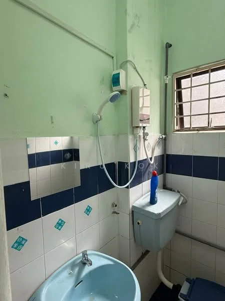 Bathroom features: green painted walls, white tiled walls with blue accents, single-bowl sink, chrome faucet, toilet, showerhead with wall-mounted holder, small window for natural light, mirror above sink, cleaning bottle on floor.
