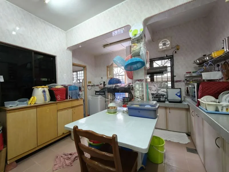 Kitchen features: white painted walls, tile flooring, wood cabinetry, kitchen island with table, stainless-steel sink, chrome pull-down faucet, microwave, refrigerator, dish rack, various kitchen utensils, window with metal grille, hanging storage rack, plastic containers, colorful cleaning supplies.