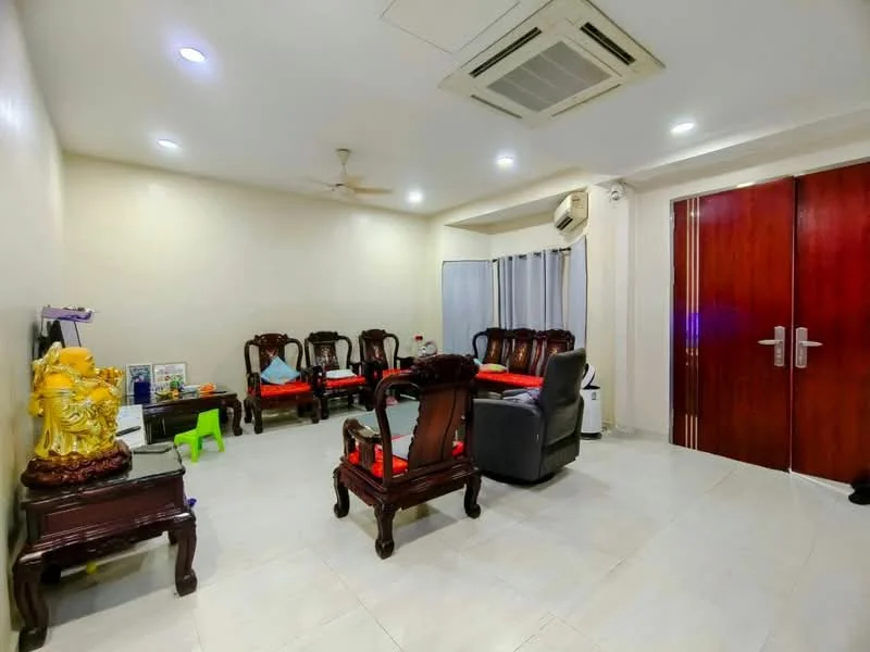 Living features: white painted walls, tile flooring, 5-blade ceiling fan, wall-mounted split AC, recessed downlights, wooden armchairs with red cushions, dark wooden coffee table, grey leather recliner, curtains, decorative statue, green children's chair; style: modern.