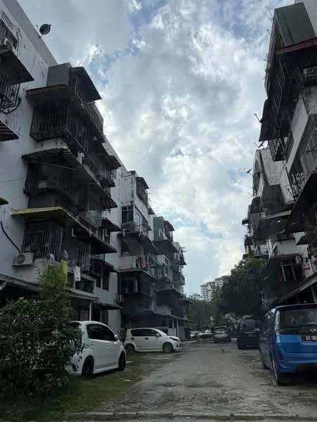 Exterior type: low-rise apartment block; features: white painted facade, balconies with metal railings, multiple storeys, visible air conditioning units, parking area with vehicles, surrounding greenery, cloudy sky, asphalt pathway; style: modern.