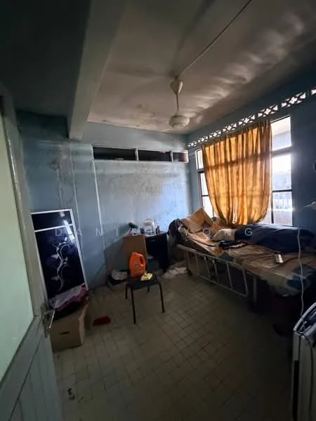 Room features: blue painted walls, ceiling fan, window with yellow curtains, tile flooring, single bed frame, messy bedding, cardboard boxes, small chair, exposed electrical outlets, wall-mounted shelf, scattered personal items.