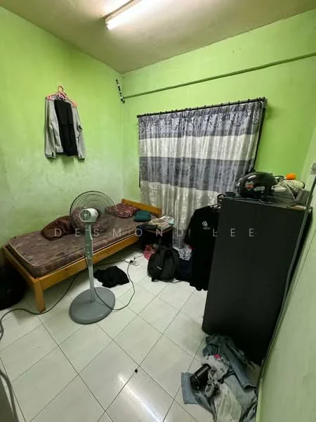 Bedroom features: green painted walls, white tiled flooring, single bed with mattress, curtains with horizontal stripes, standing fan, wardrobe, clothes on the floor, clothes hanging on a hook.