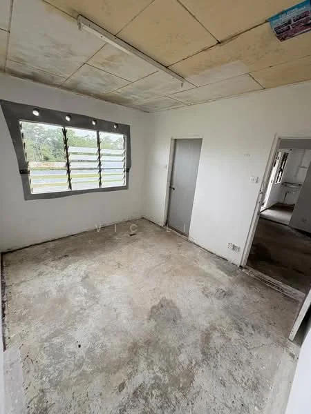 Room features: bare concrete flooring, white painted walls, sliding window with metal grille, single door, exposed ceiling with tiles, no visible lighting fixtures, no furniture, unfurnished space; view: garden.