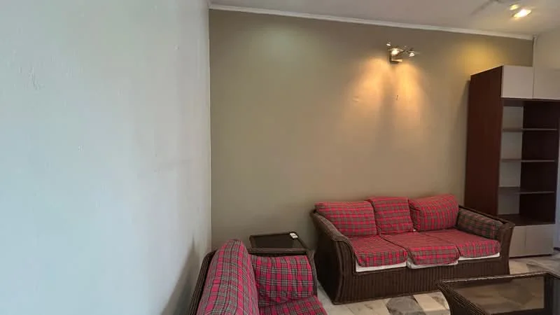 Living features: plaid fabric sofa in red and grey, 2-seater sofa, 3-seater sofa, wooden coffee table, wall-mounted light fixtures, cream painted walls, tile flooring, built-in shelving unit.