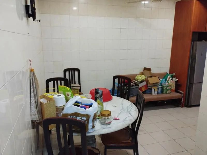 Dining features: round marble dining table, 4 wooden dining chairs, cream tiled flooring, white tiled walls, wooden cabinetry, refrigerator, sofa against the wall, various food items and containers on the table, boxes and bags on the sofa.