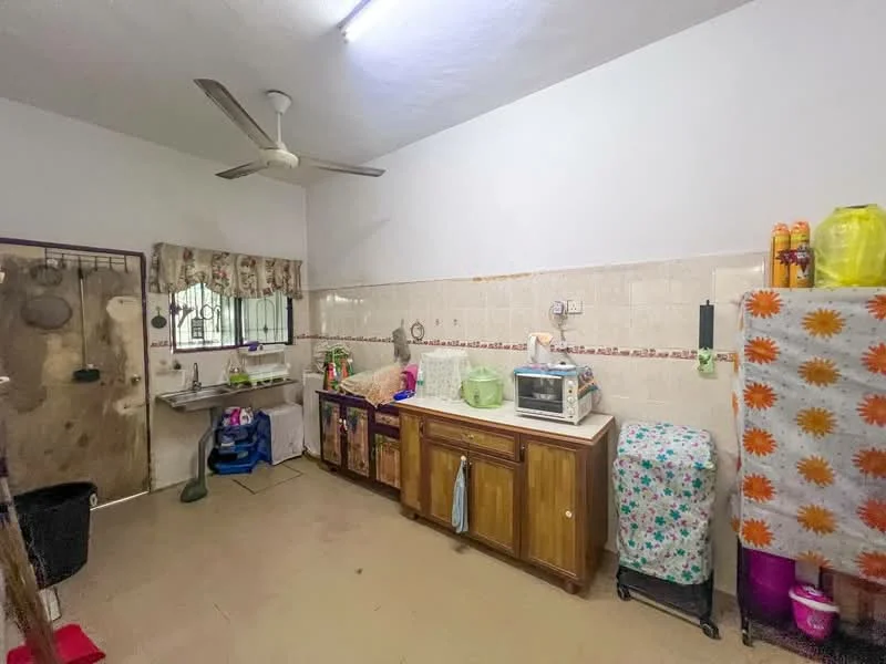 Kitchen features: wood cabinetry, single-bowl stainless-steel sink, chrome pull-down faucet, countertop with tile backsplash, microwave, refrigerator, kitchen towel hanging, ceiling fan, window with curtains, flooring with beige tiles, decorative tablecloth, cleaning supplies visible.