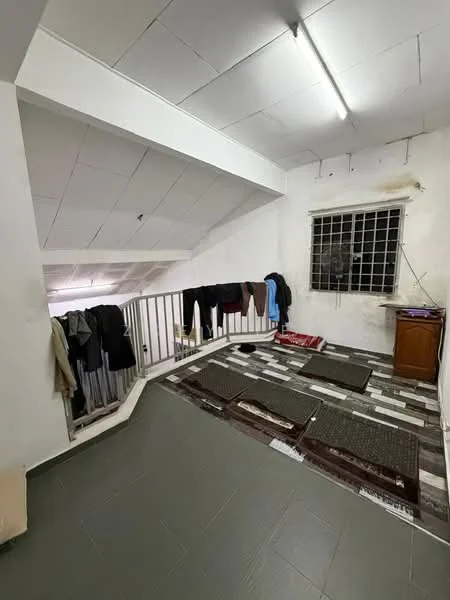 Room features: grey tiled flooring, white painted walls, exposed ceiling, large window with metal grille, wooden cabinet, clothes hanging on railing, mats on the floor, striped area rug.