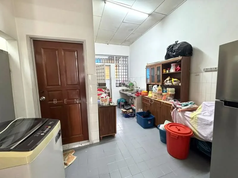 Laundry features: grey tiled flooring, white walls, wooden door, built-in wooden cabinet, washing machine, various storage containers, countertop with clutter, sink, refrigerator, open shelving, plastic bins, laundry basket.