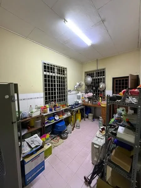 Kitchen features: pink tiled flooring, yellow painted walls, metal shelving unit, wooden cabinets, stainless-steel fridge, double-basin sink, hanging pots, various kitchen utensils, multiple containers, window with metal grilles, overhead fluorescent lighting.