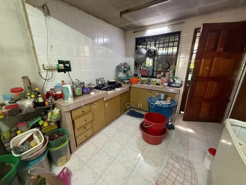 Kitchen features: white tiled walls, white tiled flooring, brown wooden cabinetry, pink countertop, stainless-steel sink, gas stove, microwave, refrigerator, various kitchen appliances, multiple pots and pans, plastic storage containers, open shelving, window with metal grilles, door leading outside.
