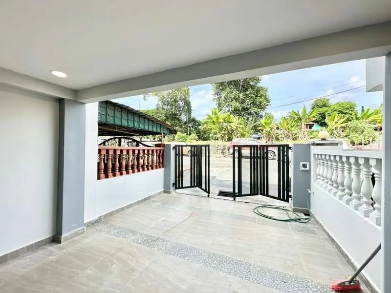 Room features: grey tiled flooring, white painted walls, sliding glass door, black metal gate, outdoor view, decorative railing, greenery visible outside, concrete ceiling, hosepipe on floor; style: modern; view: garden.