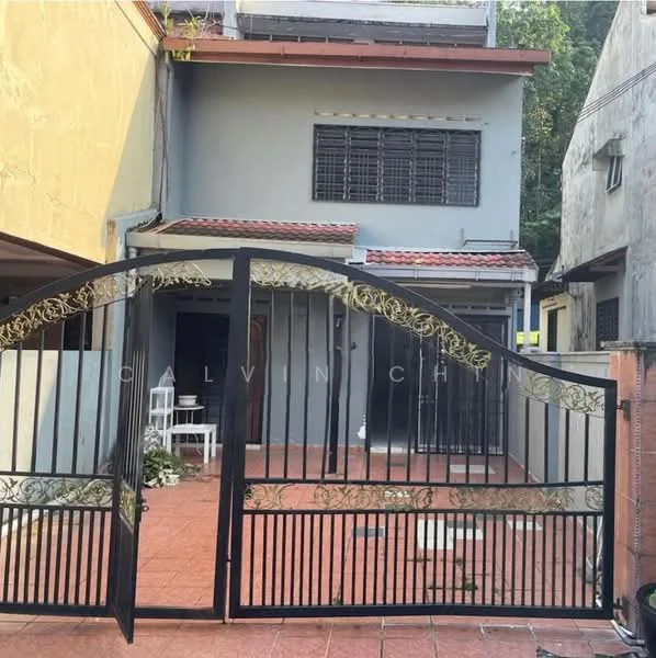 Exterior type: semi-detached house; features: black wrought iron gate with decorative design, red tiled flooring, grey painted facade, two-storey structure, windows with metal grilles, small outdoor seating area visible, surrounded by greenery; style: modern.