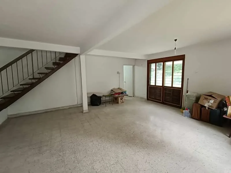 Room features: white painted walls, concrete flooring, staircase with metal railing, large windows with wooden frames, door leading to outside, unfurnished space, various boxes and items, natural light from windows.