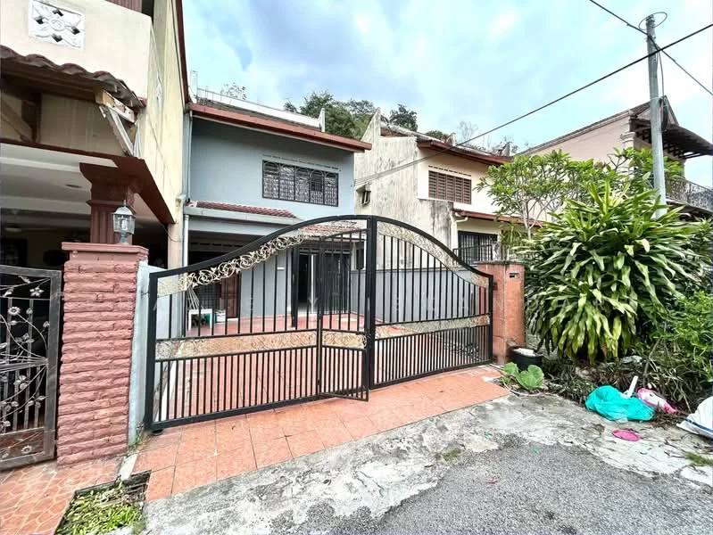 Exterior type: semi-detached house; features: black metal gate, red brick fence, tiled driveway, manicured landscaping, tropical plants, two-storey structure, front porch, grey painted facade, windows with grilles, paved walkway; style: modern.
