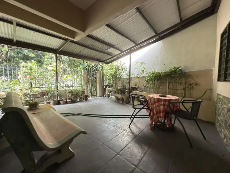 Room features: covered patio, grey tiled flooring, wooden bench, round dining table with checkered tablecloth, black metal chairs, potted plants, green garden hose, exposed beams, natural light from outside, walls with light paint, decorative stone wall; style: modern; view: garden.
