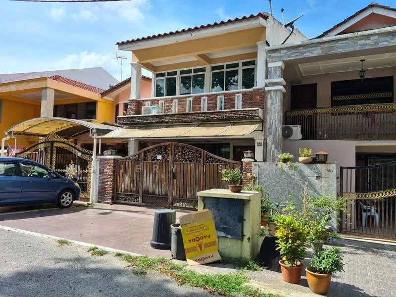 Exterior type: linked terrace house; features: two-storey building, brick facade with stone cladding, front gate with decorative metalwork, covered car porch, manicured garden with potted plants, windows with grilles, balcony on the upper floor, driveway with interlocking pavers, visible air conditioning unit, surrounded by other residential buildings; style: modern.