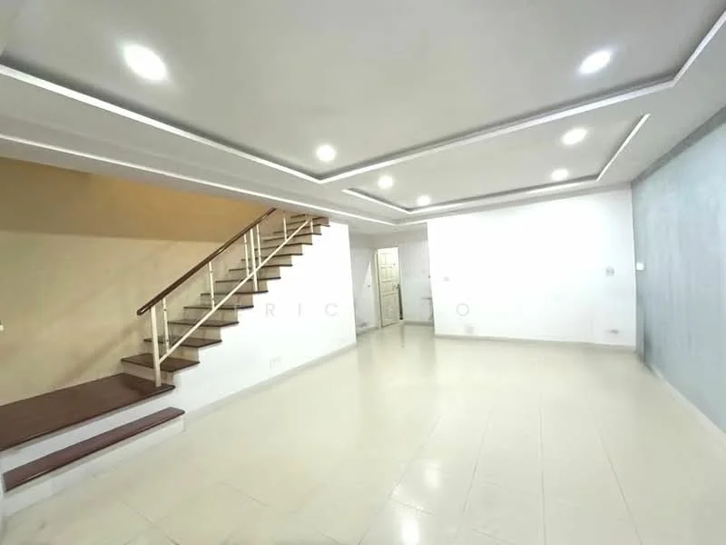Room features: white painted walls, cream tiled flooring, recessed LED downlights, staircase with wooden handrail, open layout, ceiling with cove lighting, large wall space for decor, doorway leading to another room; style: modern.