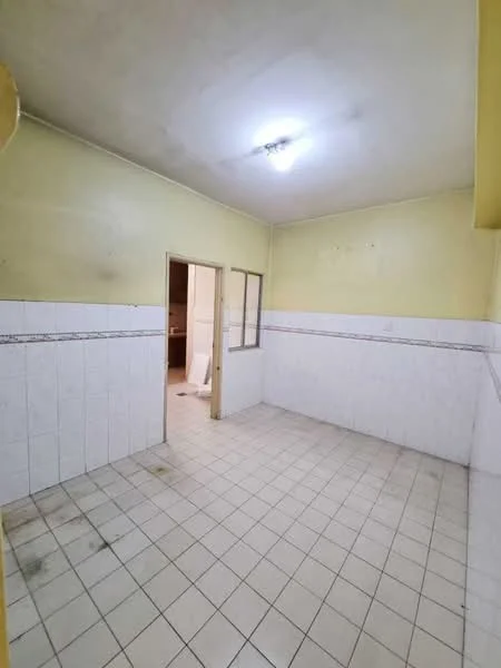 Room features: yellow painted walls, white tiled wall cladding, white ceramic floor tiles, fluorescent ceiling light, single door leading to another room, window with no visible treatment, plain ceiling, no visible furniture or appliances.