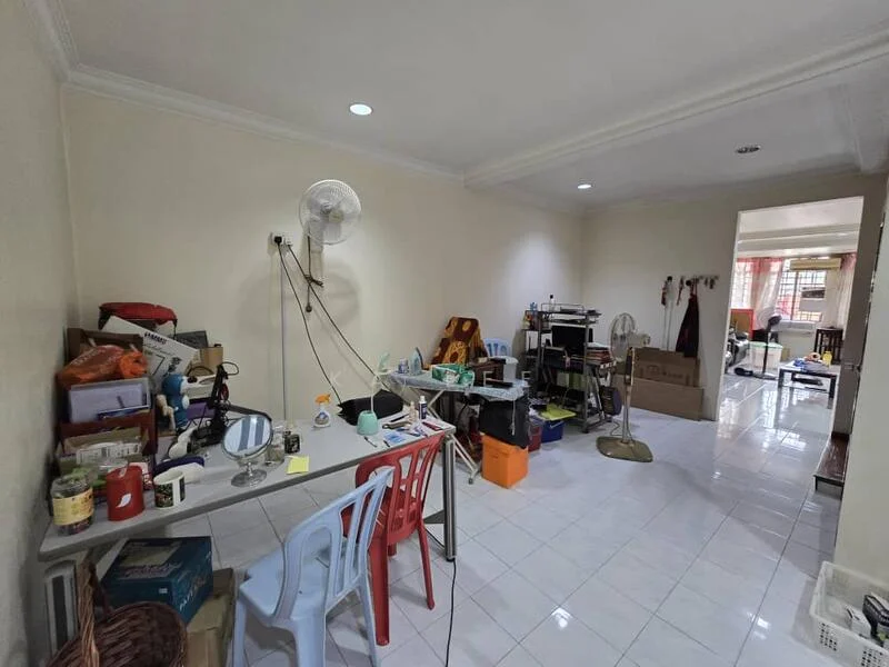 Room features: white painted walls, glossy white tile flooring, ceiling fan, table with various items, plastic chairs in red and blue, multiple boxes and storage containers, mirror on the table, exposed electrical outlets, light fixtures in ceiling, open layout.