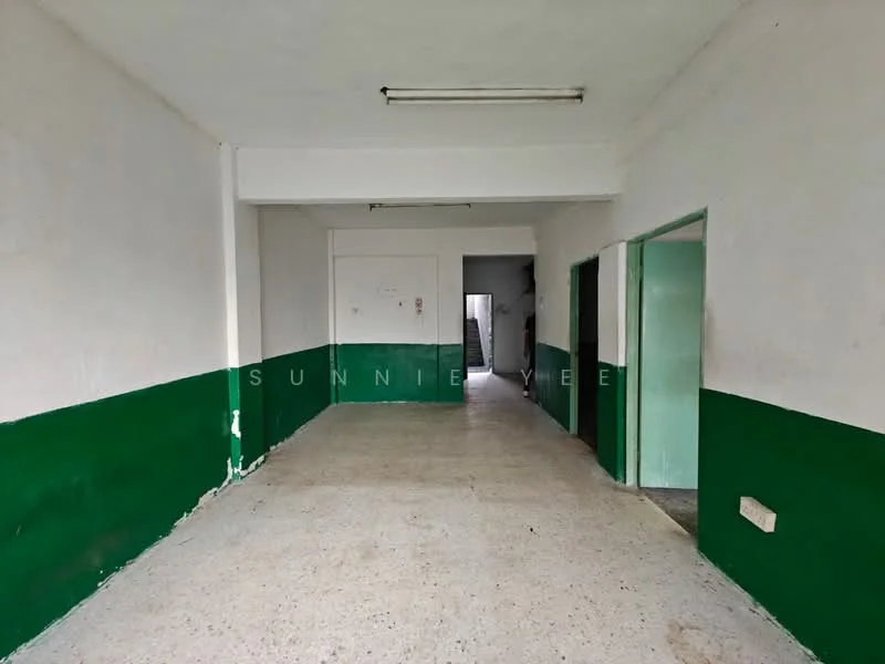 Room features: white painted walls, green painted accent wall, concrete flooring, fluorescent ceiling lights, doorway leading to another room, doorway leading to staircase, no visible furniture or decor; style: minimalist.