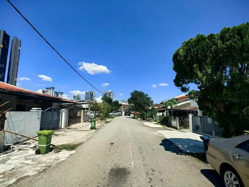 Exterior features: paved road, street lined with trees, residential houses on both sides, green garbage bins, clear blue sky, city skyline in background.