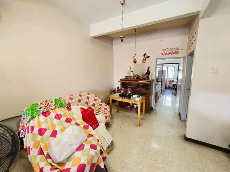 Living features: beige painted walls, polished concrete flooring, ceiling light fixture, 3-seater sofa with colorful patterned throw, wooden side table, decorative items on table, open layout to adjacent room.