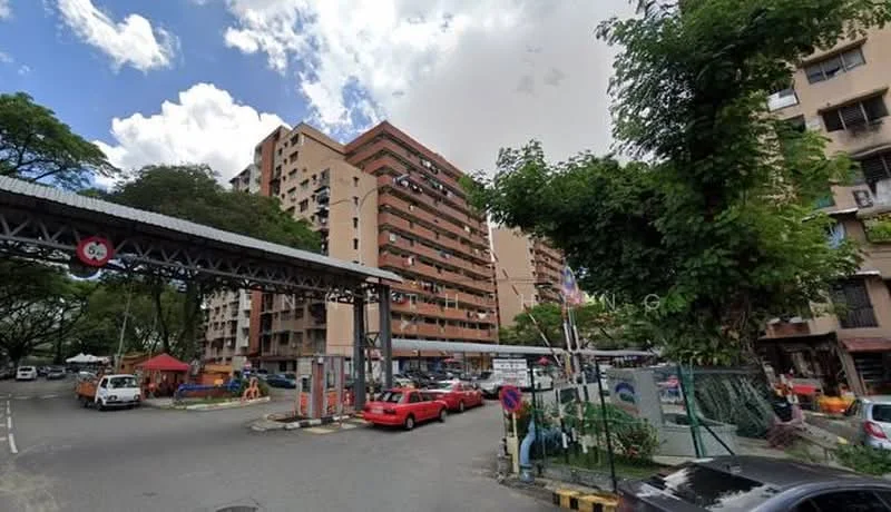 Exterior type: low-rise apartment block; features: multi-storey building, red brick facade, balconies on upper floors, surrounded by greenery, parking area visible, entrance gate with security, road access, nearby street vendors, trees lining the street; style: modern.