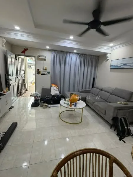 Living features: grey fabric sectional sofa, round coffee table, white painted walls with crown moulding, marble tile flooring, 5-blade ceiling fan with light, floor-to-ceiling curtains, wall-mounted artwork, open shelving unit, decorative items on shelves, visible entrance door, light fixtures, cluttered space with personal items; style: modern.