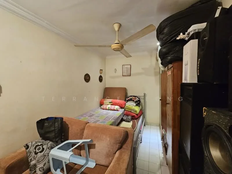 Room features: cream painted walls, white tiled flooring, ceiling fan, double bed with bedding, sofa with fabric upholstery in beige, wooden wardrobe, stacked blankets and towels, plastic chair, speakers, decorative wall plates.