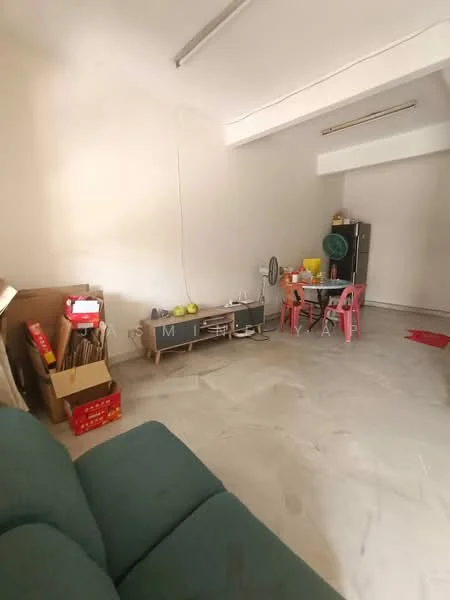 Room features: light-colored walls, marble flooring, sofa in green fabric, wooden shelving unit, dining table with pink chairs, ceiling fan, various boxes and items stored, floor lamp, small fan.