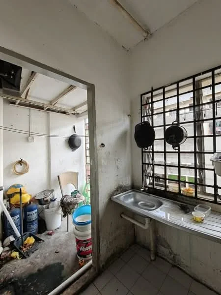 Room features: white painted walls, exposed ceiling beams, tile flooring, single-bowl stainless-steel sink, metal window grilles, hanging pots, plastic buckets, cleaning supplies, garbage bags, storage containers.