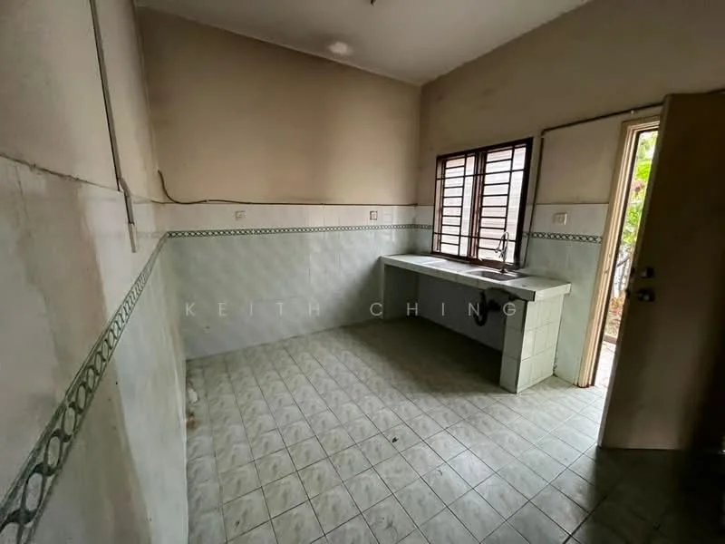 Kitchen features: white tiled walls, green decorative tile border, grey tiled flooring, single-bowl sink, window with wooden frame, door leading outside, countertop with storage underneath, no visible appliances.