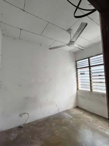 Room features: white painted walls, concrete flooring, 5-blade ceiling fan, sliding windows with metal grilles, exposed electrical wiring, natural light from windows.