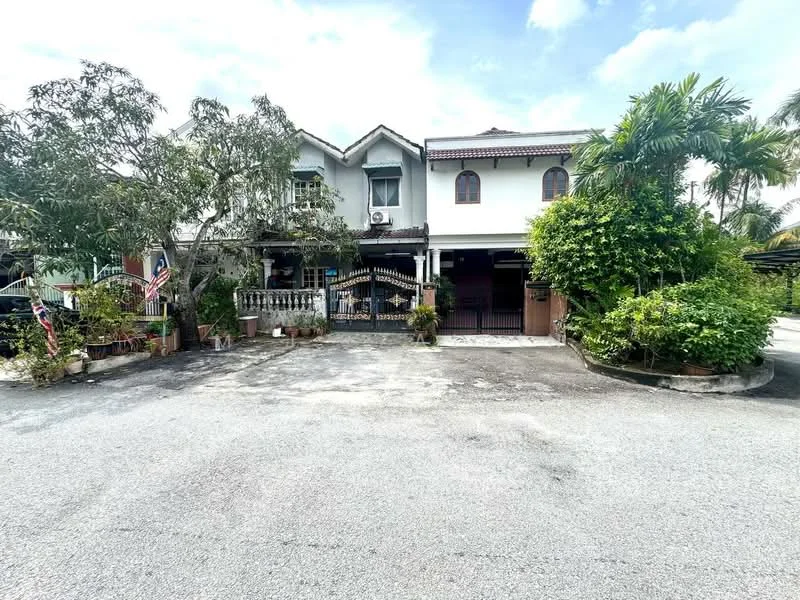 Exterior type: linked terrace house; features: two-storey building, white painted facade, red tiled roof, front porch area, manicured garden with shrubs, potted plants at entrance, visible air conditioning unit, decorative wrought iron gate, flag poles with Malaysian flags, driveway with gravel surface; style: traditional.