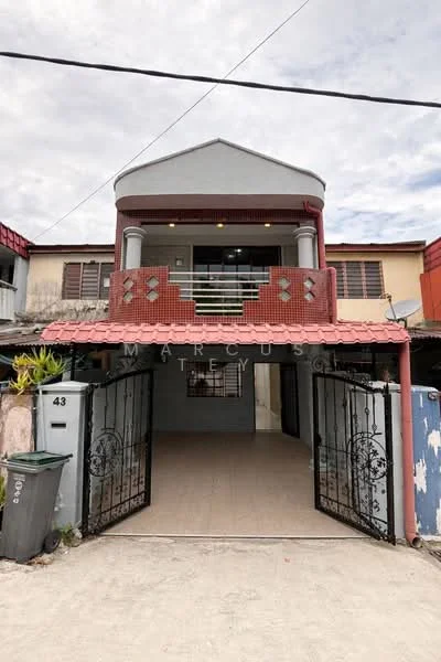 Exterior type: semi-detached house; features: two-storey building, red brick facade, covered porch area, metal gate at entrance, tiled flooring at entrance, balcony with railing on upper floor, windows with grilles, manicured plants at entrance, roof with overhang, exposed concrete walls, driveway area; style: modern.