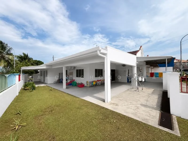 Exterior type: detached bungalow; features: white painted facade, flat roof, single-storey, manicured lawn, paved walkway, outdoor seating area with colorful bean bags, laundry area with drying rack, surrounded by greenery, fenced perimeter, car porch; style: modern.