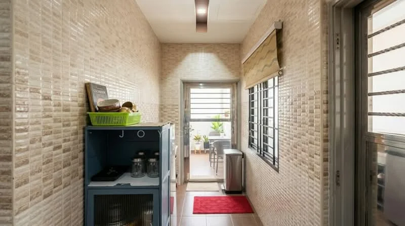 Room features: textured wall tiles in beige, cream painted walls, tile flooring in light brown, recessed ceiling lights, sliding glass door to outdoor area, window with metal grilles, small potted plants visible outside, red area rug, blue storage cabinet, metal trash bin, decorative items on cabinet; style: modern; view: garden.