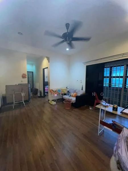 Room features: wooden flooring, ceiling fan, white painted walls, large window with grid pattern, doorway leading to another room, various furniture items including a table and chairs, baskets and miscellaneous items on the floor, light fixture on ceiling.