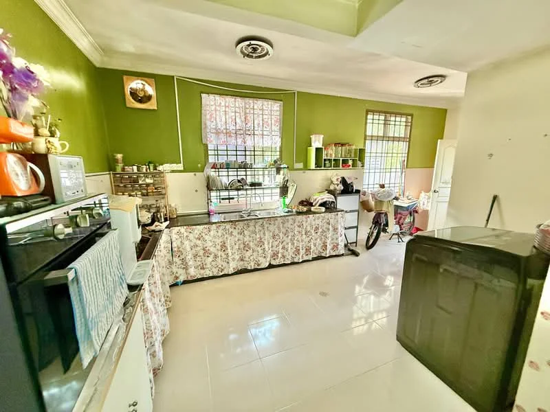 Kitchen features: green painted walls, white tiled flooring, black countertop, stainless-steel microwave, stainless-steel fridge, kitchen cabinets, sink, window with metal grills, decorative wall art, bicycle, kitchen utensils on countertop, floral tablecloth.